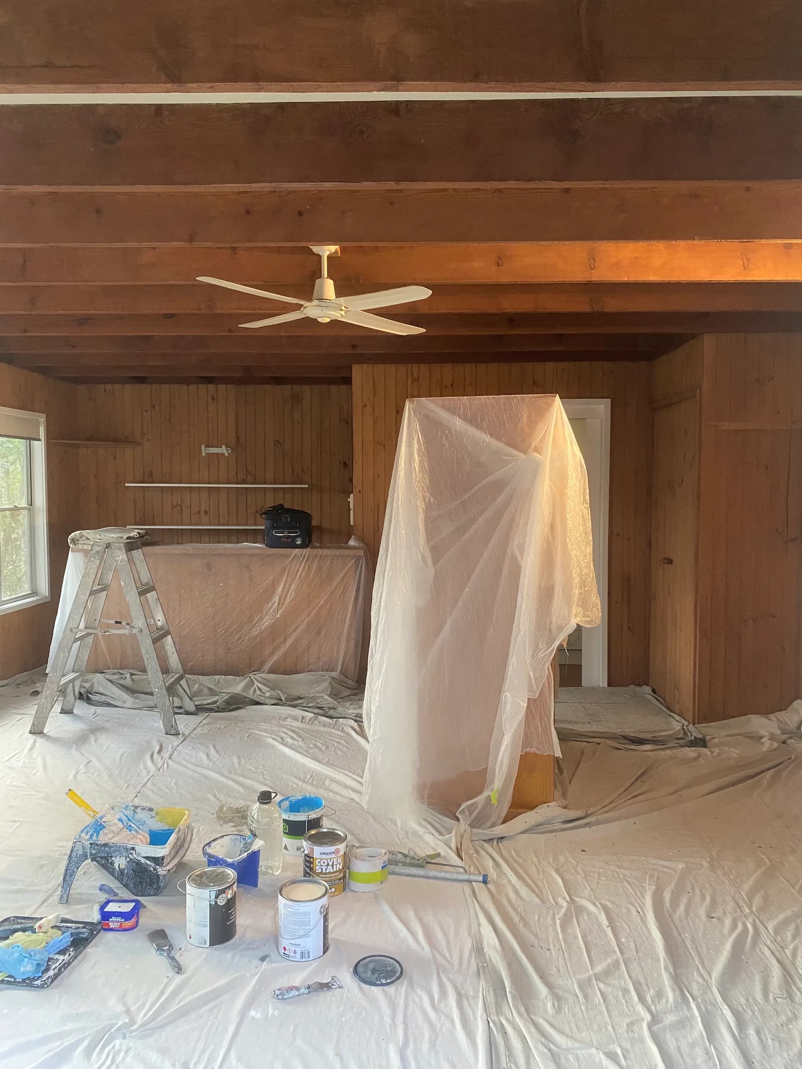 Interior painting preparation in a Sydney home with canvas drop sheets across the floor, a ladder in place and the bench fully covered